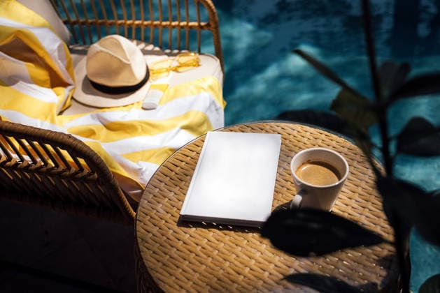 Gemütliche Atmosphäre im Freien mit einem Korbstuhl, auf dem eine gelb gestreifte Decke liegt, einem Sonnenhut, einem leeren Notizbuch und einer Tasse Kaffee am Rand eines Swimmingpools Outdoor scene with a wicker chair adorned with a yellow striped blanket, a sun hat, a blank notebook, and a cup of coffee next to a swimming pool (License=RF) Copyright: xZoonar.com DashaxPetrenkox 25107241