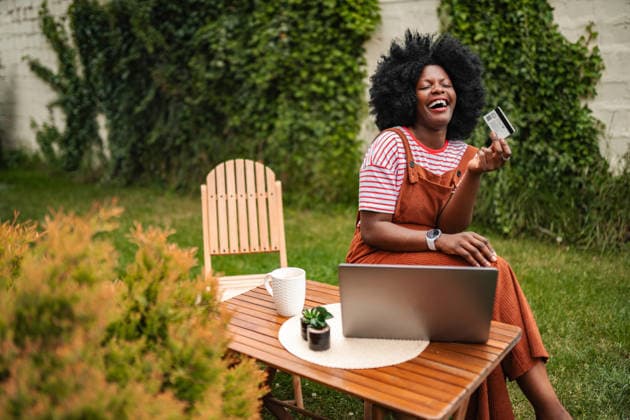 Eine junge Frau lacht und hält eine Kreditkarte für Online-Einkäufe in der Hand Happy young adult woman laughing while shopping online with credit card and laptop outdoors (License=RF) ,model released, Symbolfoto Copyright: xZoonar.com JelenaxCvetkovicx 25122372 ,model released, Symbolfoto ,property released