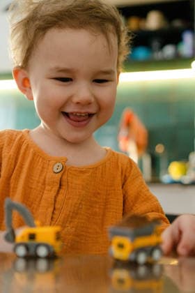 Ein Kind lächelt, während es mit einem Spielzeugbagger spielt Child smiling while playing with toy excavator at kitchen table. Toddler enjoying toy with joyful happiness and cheerful delight indoors. Happy kid beaming with toy vehicle having fun at home warmly (License=RF) ,model released, Symbolfoto Copyright: xZoonar.com elenaxskorobogatovax 25127943 ,model released, Symbolfoto ,property released