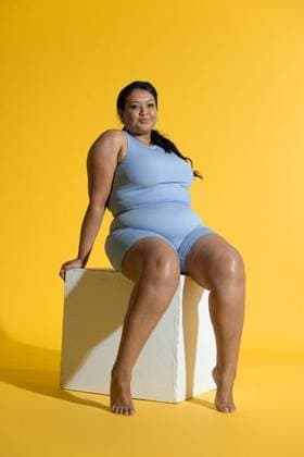 Indian woman sitting on white cube in studio with yellow backdrop, wearing light blue biker shorts, model released, property released, 27.06.2025 06:00:00, 6961327 Copyright: xIDS-260602_3xcreatorid:x0x 6961327