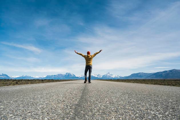 Walking with arms outstretched on an open road in Patagonia model released, Symbolfoto, UUF36820