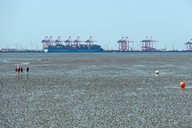 Blick vom Friesenstrand im Nordseebad Tossens, einem Ortsteil der Gemeinde Butjadingen im Landkreis Wesermarsch (Niedersachsen), auf die Nordseebucht Jadebusen mit trockenfallendem Watt. Im Hintergrund der Tiefwasserhafen Jade-Weser-Port (JWP) Wilhelmshaven. Das Wattenmeer gehört zum UNESCO-Weltnaturerbe. *** View from Friesenstrand beach in the North Sea resort of Tossens, a district of the municipality of Butjadingen in the district of Wesermarsch in Lower Saxony, of the North Sea bay of Jade Bay with dry mudflats In the background is the deep-water port Jade Weser Port JWP Wilhelmshaven The Wadden Sea is a UNESCO World Heritage Site