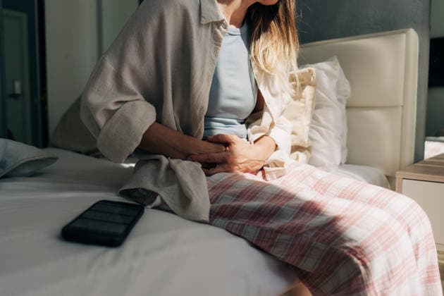 Eine nicht identifizierbare Frau sitzt auf dem Bett und hält sich den Bauch ? Bauchschmerzen, Menstruation und Blähungen. Ein Handy mit einer App für den Menstruationszyklus. Unrecognizable woman sitting on the bed holding her stomach - abdominal pain, menstruation and bloating. Mobile phone with menstrual cycle app. (License=RF) ,model released, Symbolfoto Copyright: xZoonar.com TITOVAxILONAx 25185171 ,model released, Symbolfoto ,property released