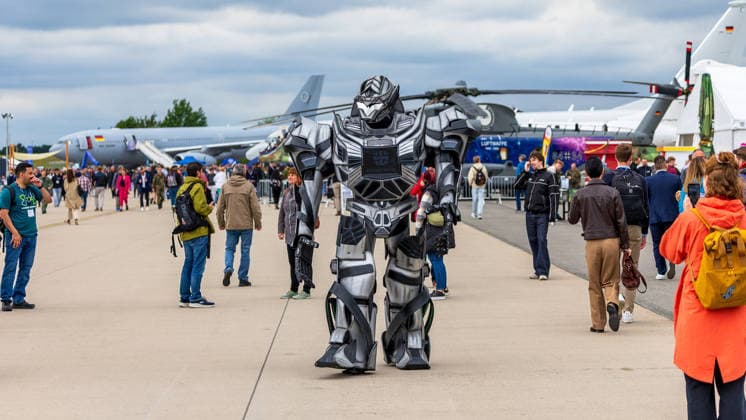 Fachbesuchertag auf ILA Berlin 2026, Berlin, 12.06.2026 Eine Person im ueberdimensionalen Roboterkostuem mit Bundeswehr-Emblem laeuft ueber das Ausstellungsgelaende der ILA. Im Hintergrund sind Militaerflugzeuge und ein Hubschrauber der Bundeswehr sowie zahlreiche Besucher sichtbar. Schöneberg Berlin ExpoCenter Airport Brandenburg Deutschland *** Trade visitor day at ILA Berlin 2026, Berlin, 12 06 2026 A person in an oversized robot costume with Bundeswehr emblem walks across the ILA exhibition grounds Military aircraft and a Bundeswehr helicopter as well as numerous visitors are visible in the background Schöneberg Berlin ExpoCenter Airport Brandenburg Germany 20260612-1V9A1881-M4000
