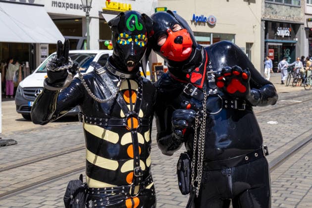 Augsburg, Bavaria, Germany June 13, 2026: Participants carrying rainbow flags and wearing colorful costumes take part in Christopher Street Day (CSD) in Augsburg. The parade through the city center promotes the rights of LGBTQ+ people as well as social diversity and tolerance. Two participants in latex costumes and puppy play masks pose *** Teilnehmerinnen und Teilnehmer mit Regenbogenflaggen und bunten Kostümen nehmen am Christopher Street Day (CSD) in Augsburg teil. Der Demonstrationszug durch die Innenstadt wirbt für die Rechte von LGBTQ+-Menschen sowie für gesellschaftliche Vielfalt und Toleranz. Zwei Teilnehmer in Latexkostümen und Puppy-Play-Masken posieren