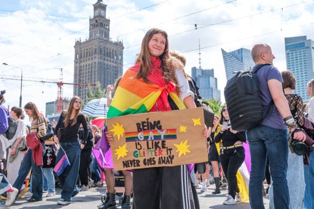 June 13, 2026, Warsaw, Masovian Voivodeship, Poland: A person wearing a rainbow flag holds a sign that reads being gay is like glitter, it never goews away during the 25th annual Warsaw LGBTQ+ Pride Parade, known in Polish as the Equality Parade. LGBTQ+ people in Poland do not have the right to same-sex civil partnerships, marriage, and child adoption, while also facing homophobia and queerphobia from a largely conservative society. Therefore, the parade is organized primarily as a march for equal rights. Warsaw Poland  - ZUMAk204 20260613_zip_k204_004 Copyright: xRomanxKozielx