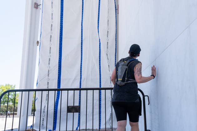 A person peeks for a view behind a tarp covering the sign for the Donald J. Trump and The John F. Kennedy Memorial Center for the Performing Arts in Washington, DC on Saturday, June 13, 2026. The Kennedy Center board voted to seek an emergency appeal to block a court order requiring the removal of President Trump s name from the Kennedy Center, but a judge denied their request.  WAP20260613052 AARONxSCHWARTZ