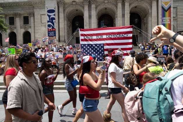June 14, 2026, New York, New York, USA: People pass by demonstrators at Rise and Resist s We Are In A State Of Emergency Flag Day anti-Trump protest on the steps of the New York Public Library (NYPL) branch on Fifth Avenue in Midtown Manhattan where a giant upside down flag is hoisted reading SAVE OUR DEMOCRACY. New York USA - ZUMAr174 20260614_znp_r174_020 Copyright: xGinaxMxRandazzox