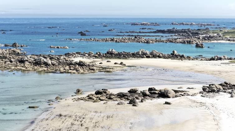 Diese eindrucksvolle Küstenansicht zeigt die weite, zerklüftete Bucht des Plage de Roc h ar Gonc. Der helle Sandstrand zieht sich entlang des flachen Ufers, das von unzähligen dunklen Granitblöcken durchsetzt ist. Weiter draußen im Meer formen langgezogene Felsbarrieren natürliche Riffe, die die Wellen des Atlantiks brechen. Das Wasser schimmert in faszinierenden Nuancen von hellem Türkis bis Tiefblau unter einem leicht dunstigen Himmel.Kerlouan, Finistère, Bretagne, Frankreich This impressive coastal view shows the wide, rugged bay of the Plage de Roc h ar Gonc. The bright sandy beach stretches along the flat shore, which is interspersed with countless dark granite blocks. Farther out in the sea, long rock barriers form natural reefs t Copyright: imageBROKER fotoping ibxwth18064298.jpg