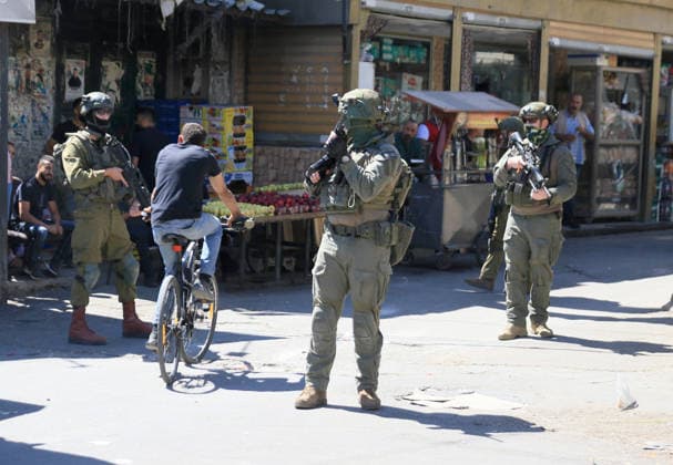 June 18, 2026, Nablus, West Bank, Palestine: A Palestinian rides his bicycle past soldiers stationed at the entrance to the market during a raid on Balata refugee camp, east of Nablus in the West Bank. Israeli forces raided the central market during a security operation. Palestinian sources said that the army arrested seven Palestinians from various neighborhoods in Nablus and its surrounding refugee camps. Nablus Palestine - ZUMAs197 20260618_aaa_s197_018 Copyright: xNasserxishatyehx