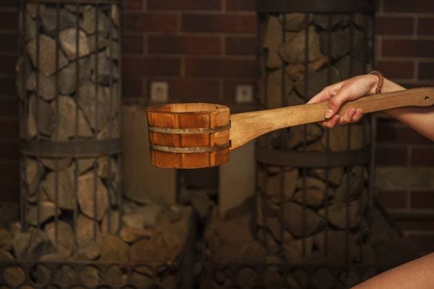 Badzubehör aus Holz mit Aromaölflasche für das Bad in der Sauna und Frau im Hintergrund Wooden bath accessories with aromatic oil bottle for bath in the sauna and woman on background Copyright: imageBROKER RuslanxOlinchuk ibxiqx17618260.jpg