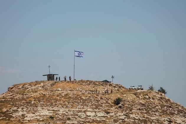 Protest Against Settlers in Dura People stand near an Israeli flag flying at a hilltop outpost in Jabal Tarousa near Dura, south of Hebron, in the occupied West Bank, on June 19, 2026. Palestinians held Friday prayers nearby to protest the establishment of the newly built Israeli settlement outpost and the seizure of land. Israeli forces later fired tear gas to suppress the gathering, allegedly causing several people, including journalists, to suffer from inhalation. Dura West Bank Palestinian Territories Copyright: xMosabxShawerx