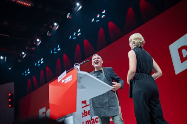 Die Parteivorsitzende Ines Schwerdtner verabschiedet ihren bisherigen Co-Vorsitzenden Jan van Aken und übergibt eine Tax the Rich-Gärtnerschütze sowie ein T-Shirt mit dem Aufdruck Jan van Sprachen;Bundesparteitag Die Linke in Potsdam - Potsdamer Parteitag 2026, Potsdam Brandenburg Deutschland Metropolis-Halle *** Party Chair Ines Schwerdtner bids farewell to her former co-chair, Jan van Aken, and presents him with a Tax the Rich garden t-shirt and a T-shirt emblazoned with Jan van Sprachen. The Left Party Federal Convention in Potsdam; 2026 Potsdam Party Convention; Potsdam, Brandenburg, Germany; Metropolis Hall,detected_source_language
