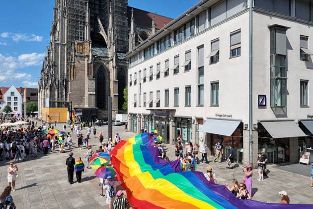 Teilnehmende tragen beim Christopher Street Day (CSD) in Ulm und Neu-Ulm eine ueber 100 Meter lange und 4,2 Meter breite Regenbogenfahne (Foto vom 20.06.2026). Die Veranstalter bezeichnen sie als die groesste Regenbogenfahne Deutschlands. Der CSD steht in diesem Jahr unter dem Motto Von Ufer zu Ufer: Wir halten zusammen! und findet zum 15. Mal statt. EDITORIAL USE ONLY *** Participants at Christopher Street Day (CSD) in Ulm and Neu Ulm are carrying a rainbow flag over 100 meters long and 4.2-meter-wide rainbow flag. Photo taken on June 20, 2026. The organizers describe it as Germany’s largest rainbow flag. This year’s CSD is themed From Shore to Shore Copyright: epd-bild ThomasxHeckmann 260620_Heckmann_Ulm_CSD_Regenbogenfahne_4197