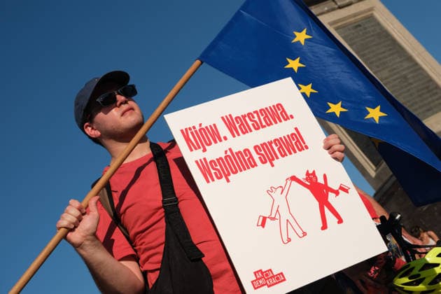 June 20, 2026, Warsaw, Masovian Voivodeship, Poland: A protester with a European Union flag holds a placard that reads Kiev, Warsaw: common cause during a demonstration on Warsaw s Castle Square for World Refugee Day. Organized under the slogan open republic, the rally was held in protest against growing xenophobia towards migrants and refugees in Poland, as well as the increasing use of anti-migrant rhetoric by Polish conservatives and far-right politicians. Warsaw Poland - ZUMAk204 20260620_zip_k204_041 Copyright: xRomanxKozielx