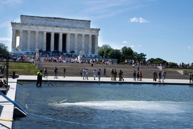 Hydrogen Peroxide is pumped into the newly renovated Lincoln Memorial Reflecting Pool to clean algae as residents and tourists walk by on the National Mall in Washington, DC on Saturday, June 20,2026. The Trump Administration awarded no-bid contracts totaling nearly $15 million to renovated Reflecting Pool but it is now filled with algae and the paint is peeling. Dozens of National Guard and other police stop people from taking the blue paint chips floating in the water, with some arrests.  WAP2026062018 PATxBENIC