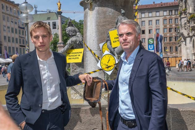 Oberbürgermeister Dominik Krause, Die Grünen, und Stadtkämmerer Christoph Frey, (rechts), zeigen am Fischbrunnen symbolisch die leere Stadtkasse her, beim bundesweiten Aktionstag Kommunalfinanzen, Münchner Aktion 5 vor 12, München, 22. Juni 2026 Deutschland, München, 22. Juni 2026, Oberbürgermeister Dominik Krause, Die Grünen, und Stadtkämmerer Christoph Frey, (rechts), zeigen am Fischbrunnen symbolisch die leere Stadtkasse her, beim bundesweiten Aktionstag Kommunalfinanzen, Münchner Aktion 5 vor 12, wollen damit auf die dramatische kommunale Finanzsituation aufmerksam machen, Finanzlage der Städte, Landkreise und Gemeinden ist dramatisch, hohe Defizite und Schulden in den Haushalten, der Aktionstag wird vom Deutschen Städtetag,