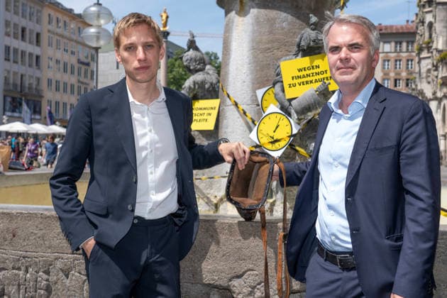Oberbürgermeister Dominik Krause, Die Grünen, und Stadtkämmerer Christoph Frey, (rechts), zeigen am Fischbrunnen symbolisch die leere Stadtkasse her, beim bundesweiten Aktionstag Kommunalfinanzen, Münchner Aktion 5 vor 12, München, 22. Juni 2026 Deutschland, München, 22. Juni 2026, Oberbürgermeister Dominik Krause, Die Grünen, und Stadtkämmerer Christoph Frey, (rechts), zeigen am Fischbrunnen symbolisch die leere Stadtkasse her, beim bundesweiten Aktionstag Kommunalfinanzen, Münchner Aktion 5 vor 12, wollen damit auf die dramatische kommunale Finanzsituation aufmerksam machen, Finanzlage der Städte, Landkreise und Gemeinden ist dramatisch, hohe Defizite und Schulden in den Haushalten, der Aktionstag wird vom Deutschen Städtetag,