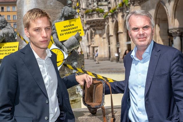 Oberbürgermeister Dominik Krause, Die Grünen, und Stadtkämmerer Christoph Frey, (rechts), zeigen am Fischbrunnen symbolisch die leere Stadtkasse her, beim bundesweiten Aktionstag Kommunalfinanzen, Münchner Aktion 5 vor 12, München, 22. Juni 2026 Deutschland, München, 22. Juni 2026, Oberbürgermeister Dominik Krause, Die Grünen, und Stadtkämmerer Christoph Frey, (rechts), zeigen am Fischbrunnen symbolisch die leere Stadtkasse her, beim bundesweiten Aktionstag Kommunalfinanzen, Münchner Aktion 5 vor 12, wollen damit auf die dramatische kommunale Finanzsituation aufmerksam machen, Finanzlage der Städte, Landkreise und Gemeinden ist dramatisch, hohe Defizite und Schulden in den Haushalten, der Aktionstag wird vom Deutschen Städtetag,