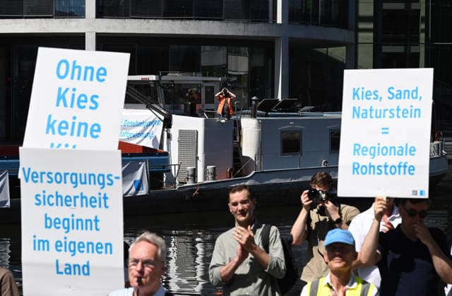 Cargo ship blocks Spree River during rally in Berlin BERLIN, GERMANY - JUNE 24: Participants gather on the banks of the Spree River as a cargo ship blocks the waterway in front of the Reichstag building during a rally organized by MIRO, the German minerals and aggregates industry association, in Berlin, Germany, on June 24, 2026. An 80-meter cargo ship loaded with construction aggregates blocked traffic on the Spree River while demonstrators called for stronger legal protection of mineral deposits and greater consideration of domestic mineral resource extraction and processing in spatial planning legislation. Volodymyr Sindieiev Anadolu Berlin Germany. Editorial use only. Please get in touch for any other usage.  Copyright: x2026xAnadoluxVolodymyrxSindieievx