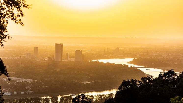 Sonnenuntergang in der Bonn Blick vom Petersberg im Siebengebirge auf Bonn bei Sonnenuntergang: Post Tower und die Hochhäuser des UN-Campus ragen aus dem goldenen Hitze-Dunst. Der Rhein mit einem Frachtschiff spiegelt das warme Abendlicht. Sommerhitze mit bis zu 35 Grad. Königswinter Petersberg Nordrhein-Westfalen Deutschland *** Sunset in Bonn: View of Bonn from Petersberg in the Siebengebirge at sunset; the Post Tower and the skyscrapers of the UN Campus rise above the golden haze of the heat; the Rhine, with a cargo ship, reflects the warm evening light; summer heat reaching up to 35 degrees; Königswinter, Petersberg, North Rhine-Westphalia Germany Copyright: xMarcxJohnx