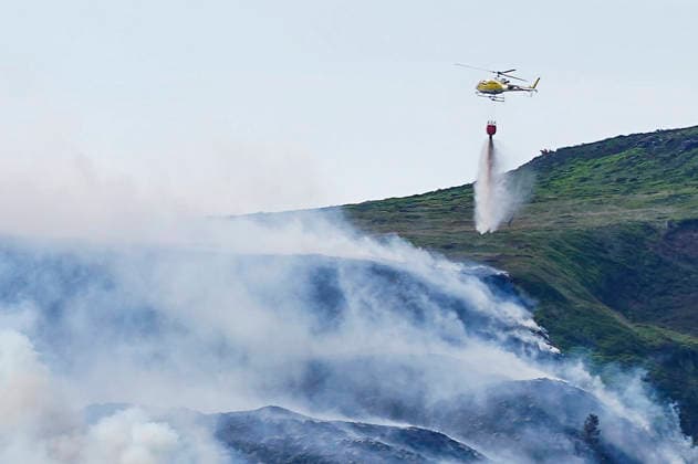 June 25, 2026, Glossop, Derbyshire, UK: Glossop, UK. A helicopter throws water above a wildfire as burns near a forest in Glossop near Wood Head Reservoir, Derbyshire. A four-day amber heat and extreme heat warning has been put in place by the Met Office, with temperatures expected to peak by the end of the week. Glossop UK  - ZUMAl94_ 20260625_zaf_l94_047 Copyright: xIoannisxAlexopoulosx