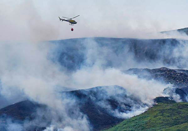 June 25, 2026, Glossop, Derbyshire, UK: Glossop, UK. A helicopter flies above a wildfire as burns near a forest in Glossop near Wood Head Reservoir, Derbyshire. A four-day amber heat and extreme heat warning has been put in place by the Met Office, with temperatures expected to peak by the end of the week. Glossop UK  - ZUMAl94_ 20260625_zaf_l94_050 Copyright: xIoannisxAlexopoulosx