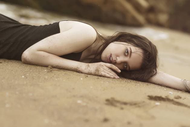 Nahaufnahme eines brünetten Mädchens, das im Sand am Meeresstrand liegt. Das Mädchen hat lange Haare und trägt ein dünnes schwarzes Kleid. es gibt große gelbe Felsen und das Meer um sie herum. Ihr Kleid ist nass. Das Mädchen ist nachdenklich Close-up of a brunette girl lying on the sand at the sea beach. the girl has long hair and is wearing a thin black dress. there are large yellow rocks and the sea around her. her dress is wet. the girl is thoughtful Copyright: imageBROKER HannaxNikulnikova ibxiqx18087402.jpg ,model released, Symbolfoto ,property released