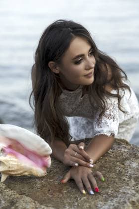 Porträt einer glücklichen, sorglosen jungen Frau am Sandstrand vor Meereshintergrund. Sie in weißem Spitzenkleid, große rosa Muschel in ihrer Nähe. Sommerurlaub, Tourismus, Sommerkleidungskonzept Portrait of happy, carefree young woman on sandy beach against sea background. she in white lace short dress, big pink shell near her. summer vacation, tourism, summer clothes concept Copyright: imageBROKER HannaxNikulnikova ibxiqx18087862.jpg ,model released, Symbolfoto ,property released