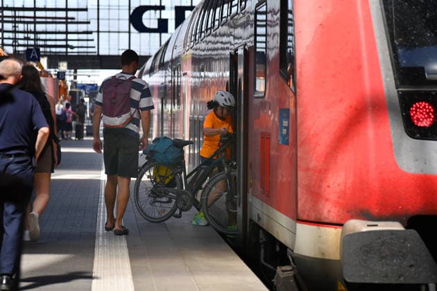 Featured photo: DB, Deutsche Bahn – Woman boarding a regional train with her bicycle; Rail passengers at Munich Central Station; DB, Die Bahn, long-distance rail service, Munich Central Station, regional train, regional rail service, locomotive