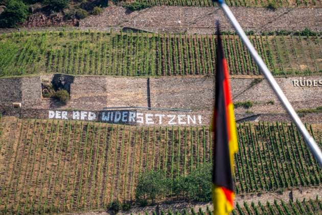 Protest Schriftzug, gegen die AfD, im Weinberg, in der Lage Rüdesheimer Roseneck, genau gegenüber von Bingen, Der AfD Widersetzen, Protest gegen die rechtsextremistische Partei, kurz vor deren Bundesparteitag in Erfurt und während einer gesellschaftlichen Diskussion üben ein Parteiverbot der rechten Partei, an eine Stützmauer geschrieben und gut weithin lesbar, der Slogan passt zu einem antifaschistischen Aktionsbündnisses das Proteste gegen die AfD und deren Parteitage organisiert, Deutschland Fahne an einem Ausflugsboot in Bingern, andere Rheinseite, Hessen, Deutschland, Der AFD Widersetzen *** Protest graffiti against the AfD in the vineyard at Rüdesheimer Roseneck, directly across from Bingen, Resisting the AfD—a protest against t
