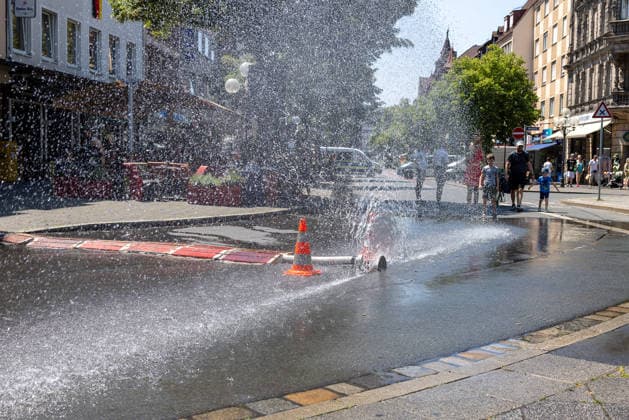 Deutschland erlebt anhaltende Hitzewelle, Nürnberg, 27.06.2026 Über einen geöffneten Feuerwehrschlauch der Berufsfeuerwehr Nürnberg am Jakobsplatz wird Wasser zum Abkühlen versprüht bei sommerlicher Hitze. Passanten kühlen sich an der improvisierten Abkühlung ab. Nürnberg Bayern Deutschland *** Germany is experiencing a prolonged heat wave, Nuremberg, June 27, 2026. Water is being sprayed from an open fire hose operated by the Nuremberg Professional Fire Department at Jakobsplatz to provide relief from the summer heat. Passersby cool off at the makeshift cooling station. Nuremberg, Bavaria, Germany 20260627-286A0392-M4000