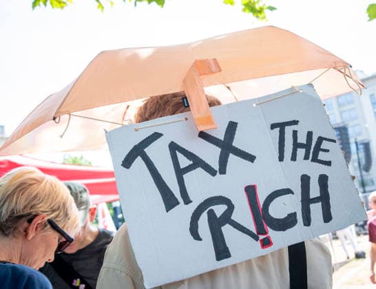 Protest gegen Sozialstaatsreform EUR, Deutschland, Berlin, 27.06.2026: Mann mit Sonnenschirm und ein Plakat mit der Aufschrift TAX THE RICH . Ein breites Bündnis aus Gewerkschaften, Sozial- und Wohlfahrtsverbänden sowie der Berliner Mieterverein protestieren gegen die geplanten Sozialstaatsreformen der Bundesregierung *** Protest Against Welfare State Reform, EUR, Germany, Berlin, June 27, 2026: A man holding a parasol and a sign reading TAX THE RICH. A broad coalition of labor unions, social and welfare organizations, and the Berlin Tenants’ Association is protesting the federal government’s planned welfare state reforms.