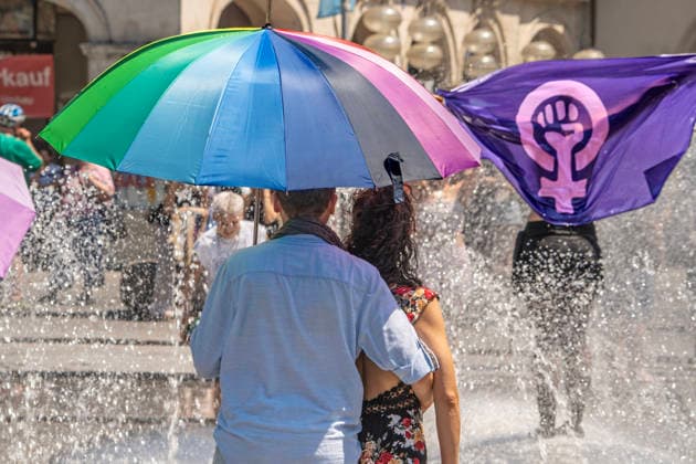 junge Frau zeigt Flagge im Stachusbrunnen, Symbol für Frauenpower und Feminismus, erhobene Faust, FLINTA, Zuschauer mit Regenbogenschirm, zufällige Szene an der Strecke des CSD 2026, große Politparade,, Hochsommer, Rekordhitze, München, 27. Juni 2026 Deutschland, München, 27. Juni 2026, junge Frau zeigt Flagge im Stachusbrunnen, Symbol für Frauenpower und Feminismus, erhobene Faust, FLINTA, Zuschauer mit Regenbogenschirm, zufällige Szene an der Strecke des CSD 2026, große PolitParade mit Hunderttausenden Zuschauern und Teilnehmern, im Rahmen der Pride Weeks, Motto Unsere Vielfalt. Unsere Stärke., Christopher Street Day, größte Demonstration von Lesben, Schwulen, Bisexuellen, trans*, inter* und queeren Menschen (LGBTIQ*) für glei