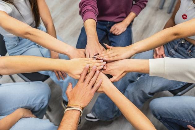 Vielfältige Gruppe junger Erwachsener, die sich in einem Kreis von oben die Hand reichen und Einheit, Teamwork und gegenseitige Unterstützung innerhalb einer multiethnischen Gemeinschaft oder eines kollaborativen Teamumfelds symbolisieren Diverse group of young adults joining hands in a top view circle, symbolizing unity, teamwork and mutual support within a multiethnic community or collaborative team setting Copyright: imageBROKER UnaixHuizi ibxuhu18092383.jpg ,model released, Symbolfoto ,property released