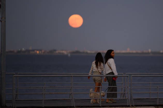 June 29, 2026, Lisbon, Portugal: People are seen walking along the banks of the Tejo River as the moon peeks over the horizon in the Lisbon sky. Strawberry Supermoon is a term derived from the traditions of the North American indigenous peoples, who called this moon by that name because it coincided with the wild strawberry harvest season. Lisbon Portugal - ZUMAs197 20260629_aaa_s197_079 Copyright: xJorgexCastellanosx