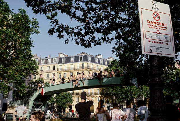 Heatwave Canal Saint Martin Paris A sign warning against swimming stands near people gathered on a footbridge over the Canal Saint-Martin in Paris, France, on June 23, 2026. As France experiences a major heatwave, people use the Canal Saint-Martin as an improvised urban beach to cool off. While the city recently opened a regulated swimming area, the extreme temperatures have led many to swim in unapproved sections of the waterway. Paris Ile de France France Copyright: xOliviaxBonnamourx
