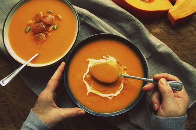 Flache Frauenhände und herbstwärmende Kürbiscremesuppe mit Croutons und Samen an Bord auf rustikalem Holzgrund, Ansicht von oben. Vegetarisches, veganes, gesundes Hausmannskostkonzept im Herbst Flat-lay of female hands and Fall warming pumpkin cream soup with croutons and seeds on board over rustic wooden background, top view. Autumn vegetarian, vegan, healthy comfort food eating concept Copyright: imageBROKER VirginijaxVaidakavic ibxvva18128860.jpg