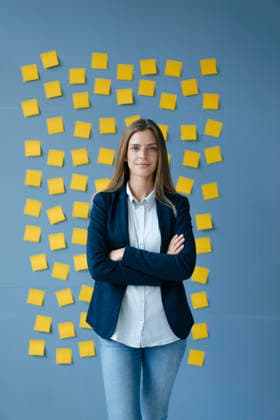 Yong businesswoman standing in front of wall, full of yellow sticky notes, with arms crossed model released, Symbolfoto property released, GUSF01776