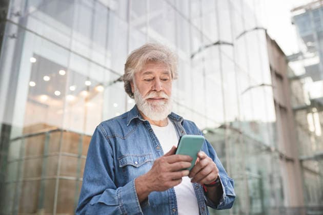White bearded man using smart phone in front of modern glass building model released, Symbolfoto, JCCMF03023
