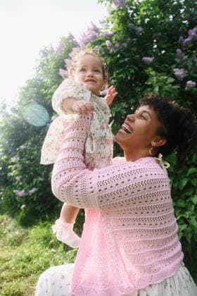 A smiling mother lifts her baby daughter outdoors by a flower bush model released, Symbolfoto, EYAF04214