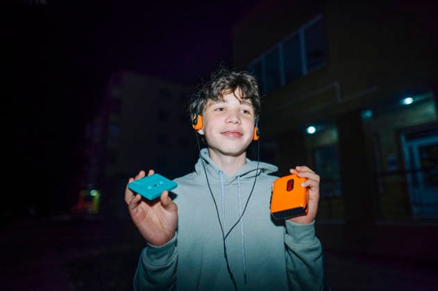 Smiling teenager walking at night listening to retro audio player model released, Symbolfoto, ANAF06189