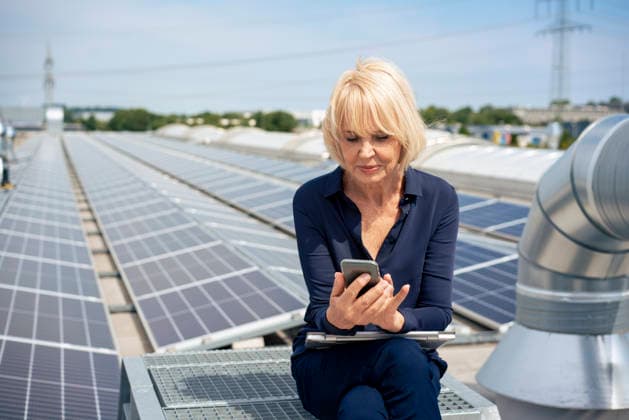 Senior businesswoman using smart phone sitting with laptop in front of solar panels model released, Symbolfoto property released, JOSEF14442