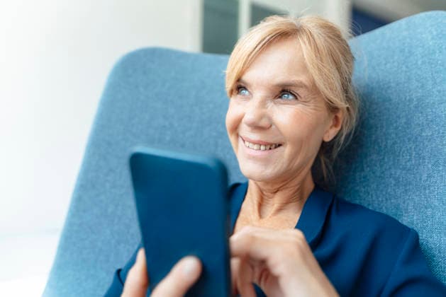 Smiling businesswoman with smart phone on armchair model released, Symbolfoto property released, JOSEF15324