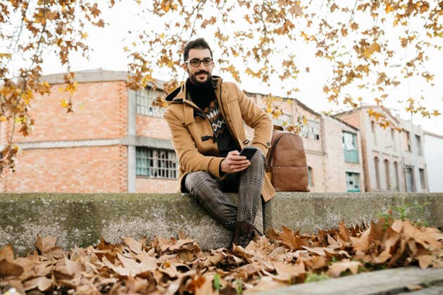 Spain, Igualada, portrait of smiling man with cell phone sitting down in the autumnal town model released, Symbolfoto, JRFF02297