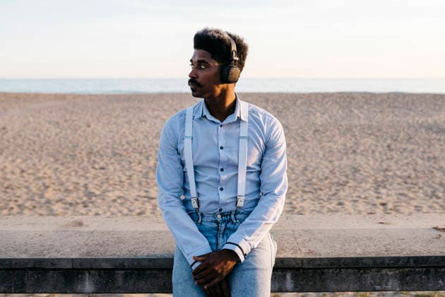 Handsome Afro man listening music through headphones while leaning against retaining wall at beach model released, Symbolfoto, JRFF05060