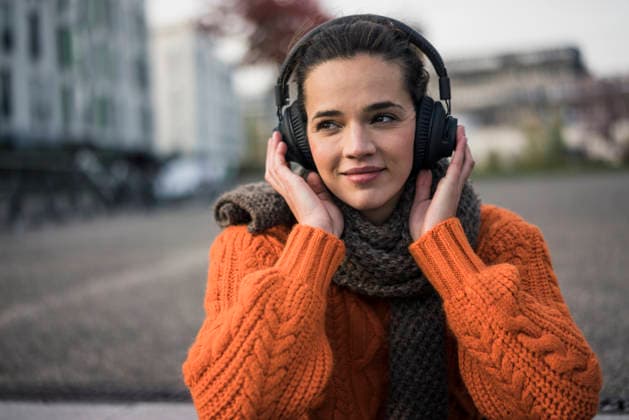 Portrait of woman wearing scarf and orange knit pullover outdoors listening music with cordless headphones model released, Symbolfoto, MOEF01878