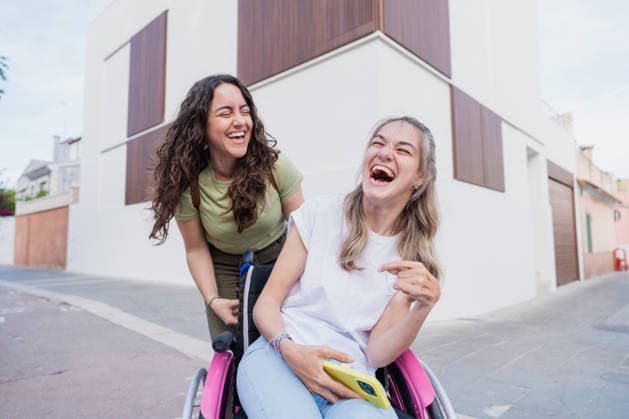 Woman pushes laughing friend in wheelchair on city street model released, Symbolfoto, MRF02710