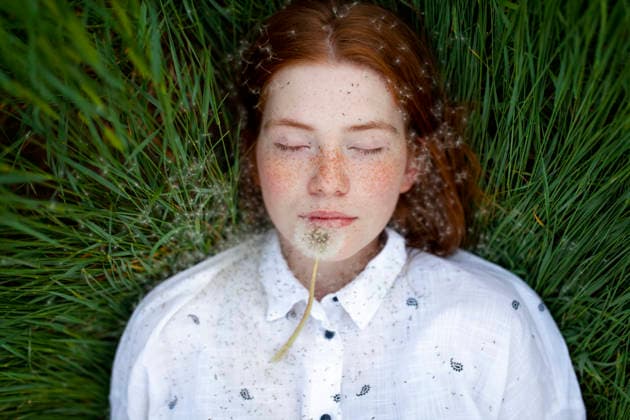 A female lies in the grass with dandelion seeds on her face model released, Symbolfoto, VCF01718