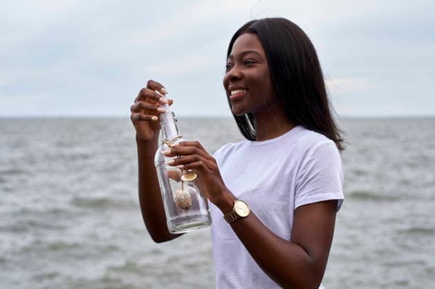 Portrait of smiling young woman in front of the sea sending message in a bottle model released, Symbolfoto property released, VEGF00082